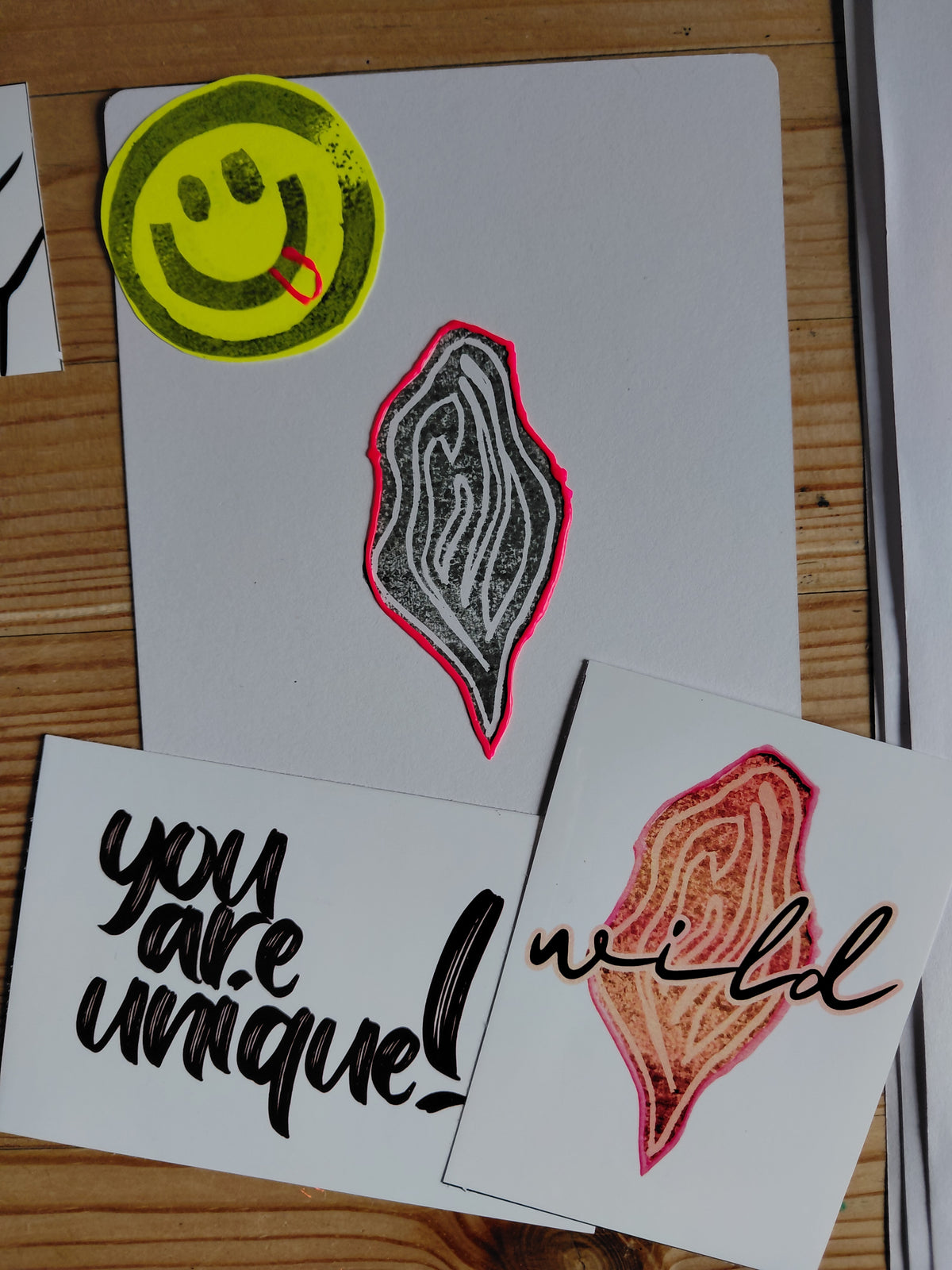 unique art print with black vulva and neon border, 2 stickers. one with a vulva and the statement wild over it, the other sticker says: You are unique!. A smiley with its tongue out stamped on yellow paper is visible on the left hand corner as well