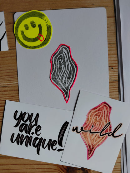 unique art print with black vulva and neon border, 2 stickers. one with a vulva and the statement wild over it, the other sticker says: You are unique!. A smiley with its tongue out stamped on yellow paper is visible on the left hand corner as well